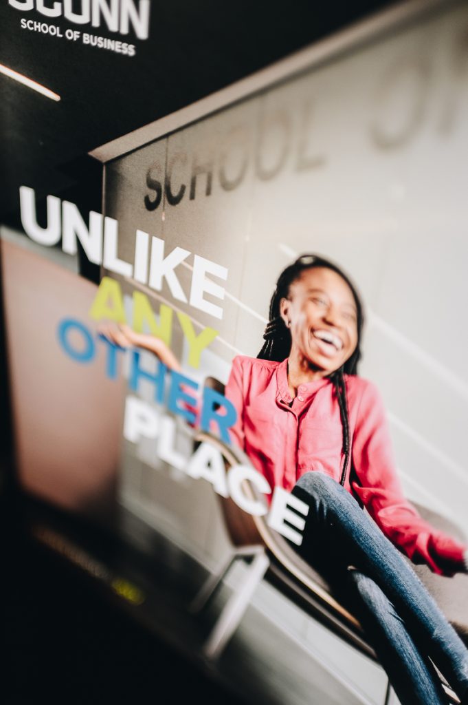 Staged photo of a UConn School of Business publication featuring a woman smiling and the text "unlike any other place."